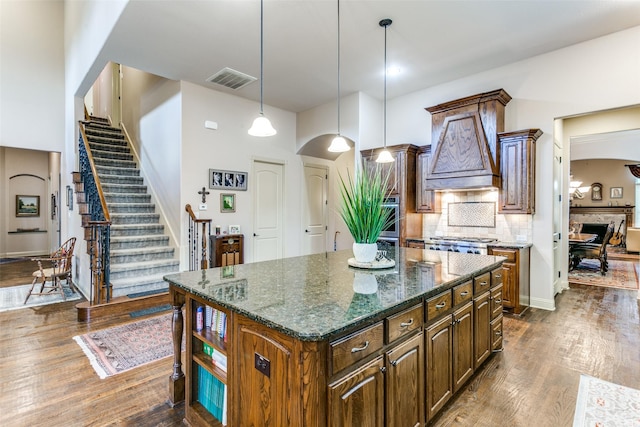 kitchen with decorative light fixtures, dark stone countertops, decorative backsplash, dark hardwood / wood-style floors, and a kitchen island