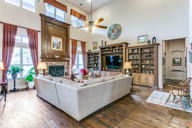 living room featuring a towering ceiling, a fireplace, ceiling fan, and dark hardwood / wood-style floors