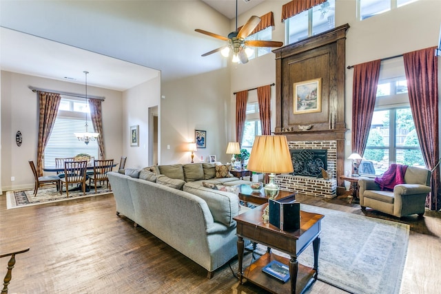 living room featuring a towering ceiling, a brick fireplace, ceiling fan, and dark hardwood / wood-style flooring