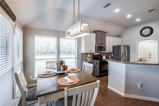 kitchen featuring vaulted ceiling, stainless steel appliances, dark stone counters, pendant lighting, and white cabinets