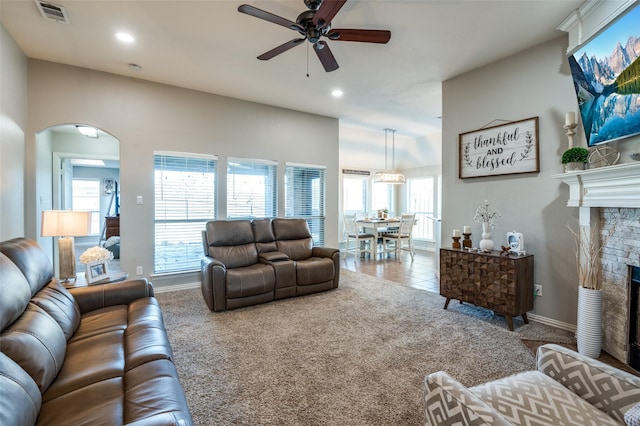 living room featuring light carpet, ceiling fan, and a stone fireplace