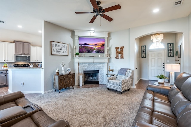 living room featuring a stone fireplace, light carpet, and ceiling fan with notable chandelier