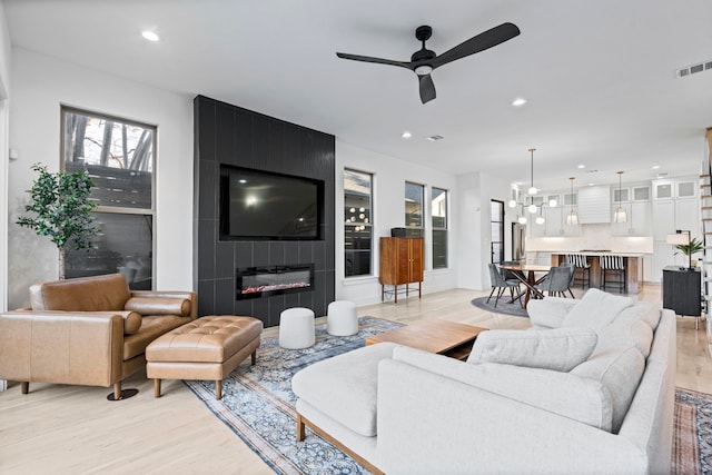 living room with a tile fireplace, light wood-type flooring, and ceiling fan