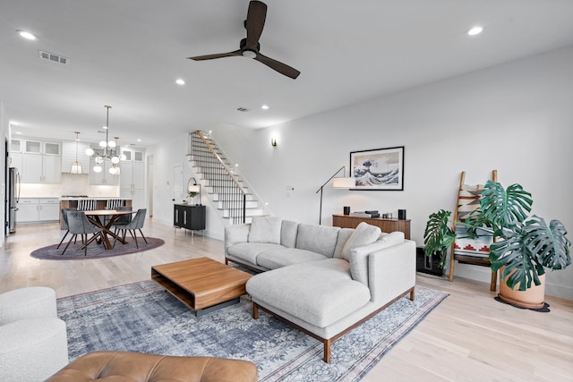 living room with light hardwood / wood-style floors and ceiling fan with notable chandelier