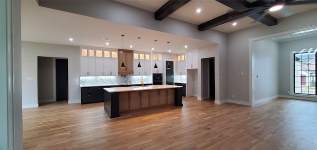 kitchen with light hardwood / wood-style flooring, decorative light fixtures, a spacious island, white cabinets, and beamed ceiling