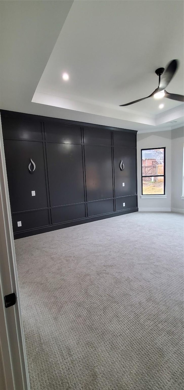 unfurnished bedroom with light colored carpet, ceiling fan, and a tray ceiling