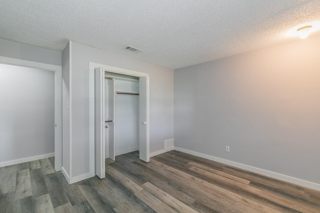 unfurnished bedroom featuring a textured ceiling, dark hardwood / wood-style flooring, and a closet