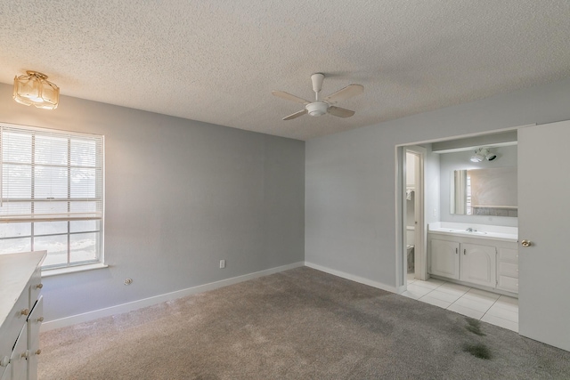 unfurnished bedroom featuring connected bathroom, a textured ceiling, ceiling fan, and light colored carpet