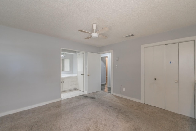 unfurnished bedroom featuring a closet, light carpet, ceiling fan, a textured ceiling, and ensuite bathroom