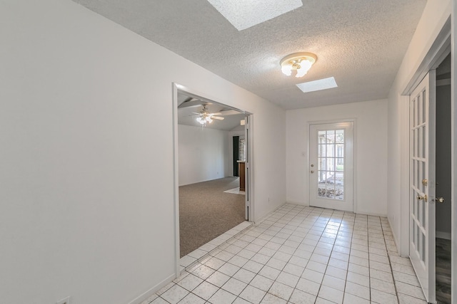 interior space with a textured ceiling, ceiling fan, light tile patterned floors, and a skylight