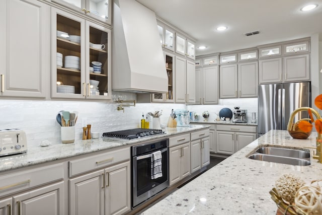 kitchen featuring light stone counters, stainless steel appliances, custom range hood, and sink