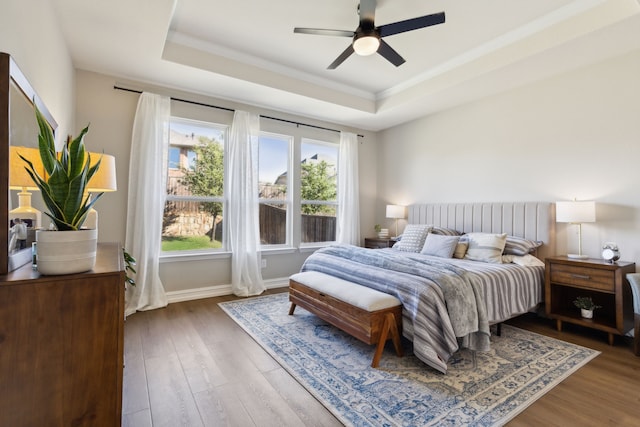 bedroom with hardwood / wood-style flooring, ceiling fan, a tray ceiling, and ornamental molding