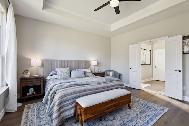 bedroom featuring connected bathroom, ceiling fan, a tray ceiling, crown molding, and dark wood-type flooring