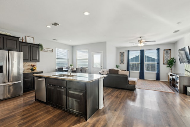 kitchen featuring a healthy amount of sunlight, a kitchen island with sink, backsplash, appliances with stainless steel finishes, and sink