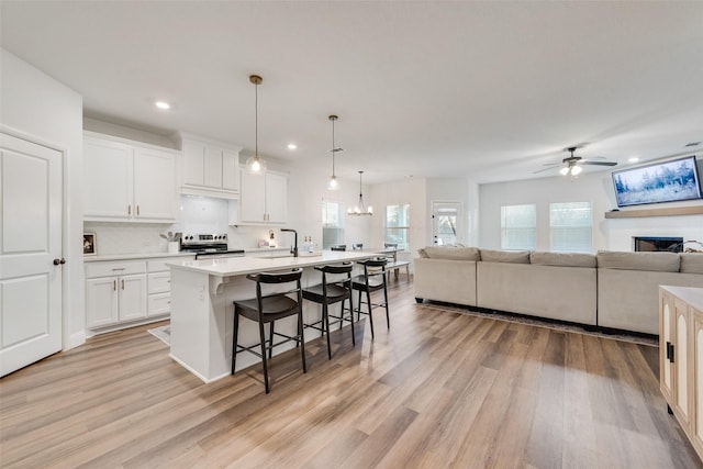 kitchen with white cabinets, a kitchen bar, an island with sink, hanging light fixtures, and stainless steel electric range