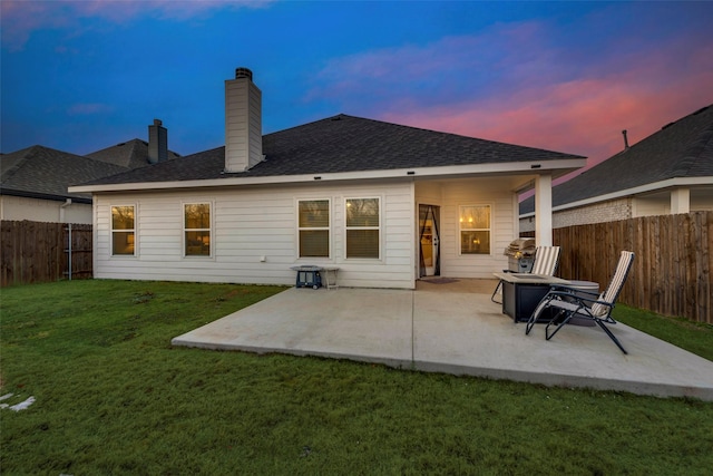 back house at dusk featuring a patio area and a yard