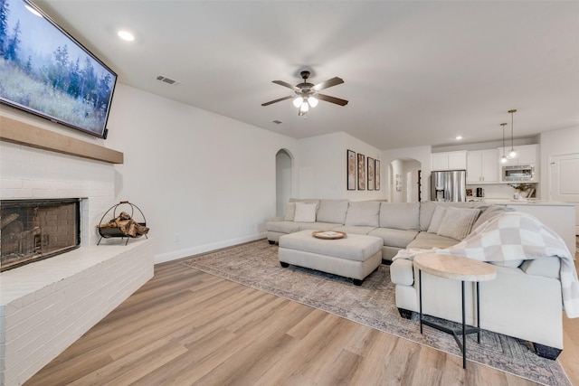 living room with ceiling fan, light wood-type flooring, and a fireplace