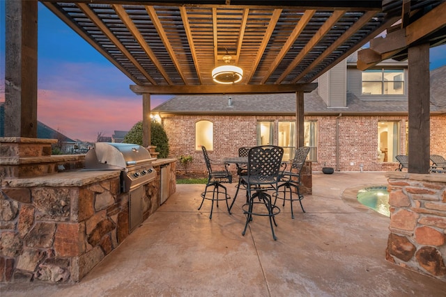 patio terrace at dusk featuring an outdoor kitchen, a pergola, and a grill