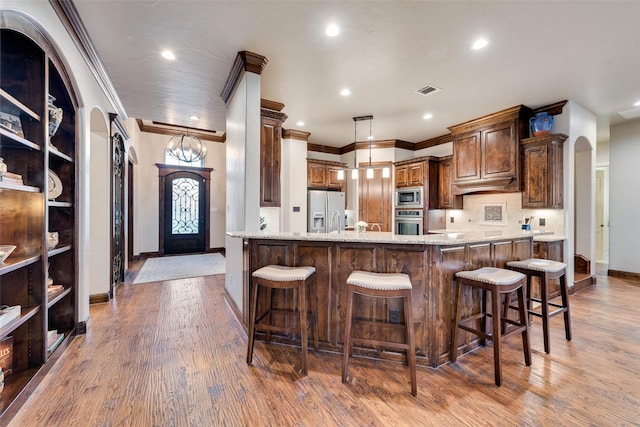 kitchen with hardwood / wood-style flooring, a breakfast bar area, light stone countertops, pendant lighting, and appliances with stainless steel finishes