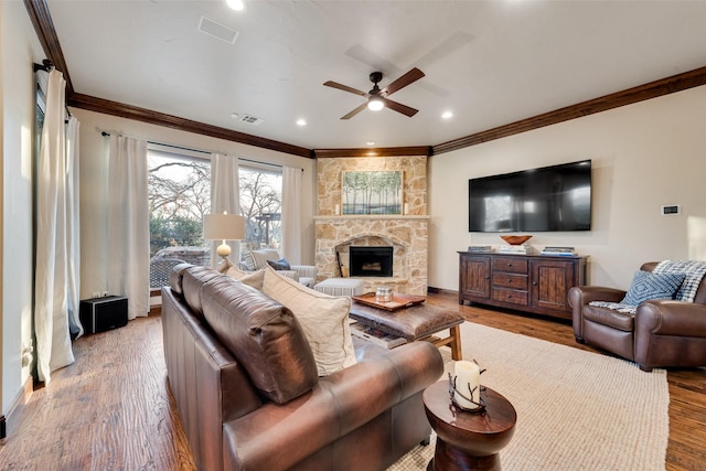 living room with light wood-type flooring, ceiling fan, crown molding, and a stone fireplace