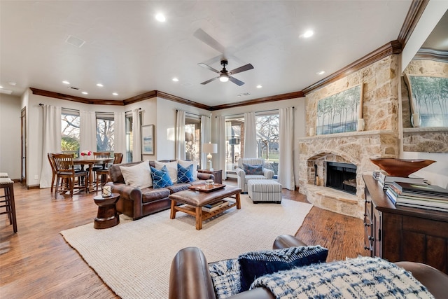 living room featuring ceiling fan, light hardwood / wood-style flooring, a stone fireplace, and crown molding