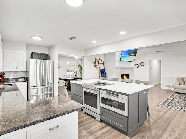 kitchen with dark stone countertops, gray cabinetry, stainless steel appliances, a center island, and white cabinets