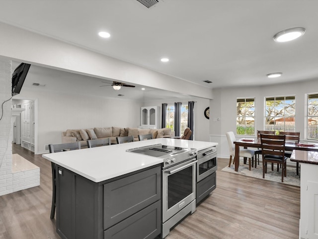 kitchen with ceiling fan, a brick fireplace, high end stove, a kitchen island, and light hardwood / wood-style flooring