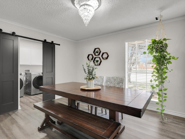 dining space with independent washer and dryer, a textured ceiling, light wood-type flooring, a barn door, and ornamental molding