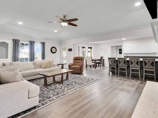 living room featuring ceiling fan, light wood-type flooring, ornamental molding, and lofted ceiling