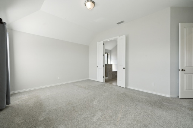 unfurnished bedroom featuring ensuite bath, carpet, and vaulted ceiling