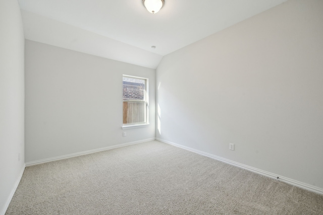 carpeted spare room with vaulted ceiling