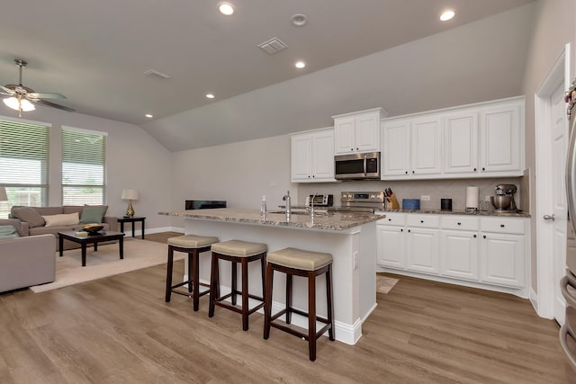 kitchen featuring a center island with sink, appliances with stainless steel finishes, vaulted ceiling, and white cabinetry