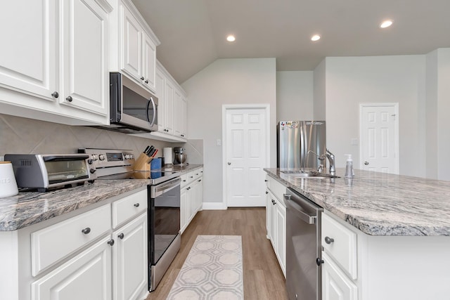 kitchen with stainless steel appliances, a center island with sink, lofted ceiling, white cabinets, and sink