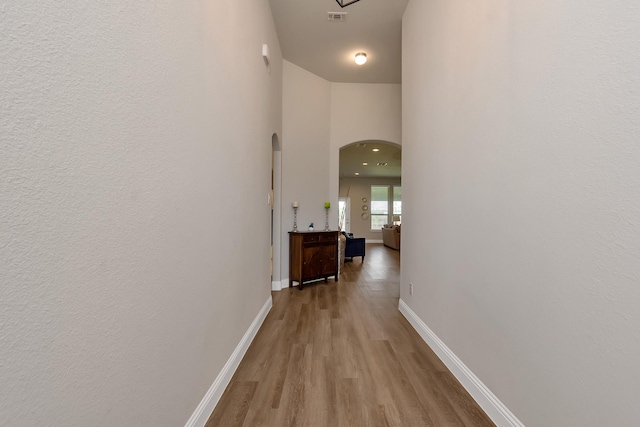 hallway with light hardwood / wood-style floors and a towering ceiling