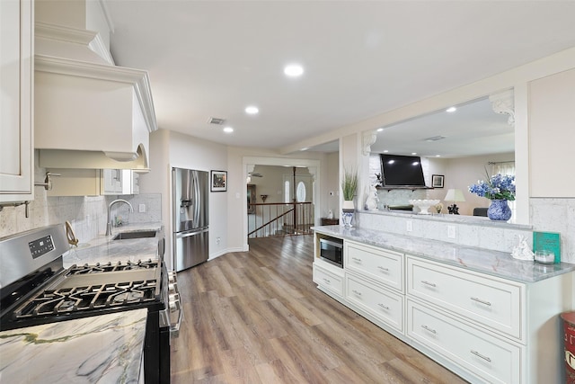 kitchen with white cabinetry, stainless steel appliances, sink, backsplash, and light stone counters