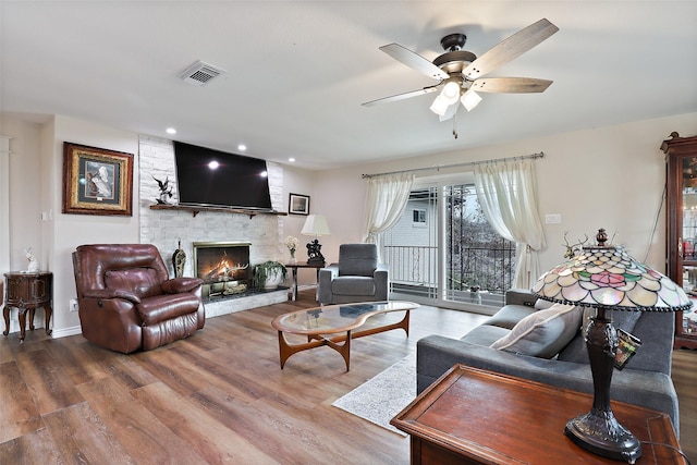 living room with ceiling fan, hardwood / wood-style flooring, and a stone fireplace