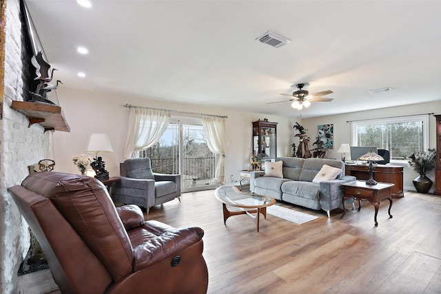 living room featuring ceiling fan, a healthy amount of sunlight, light hardwood / wood-style flooring, and a stone fireplace