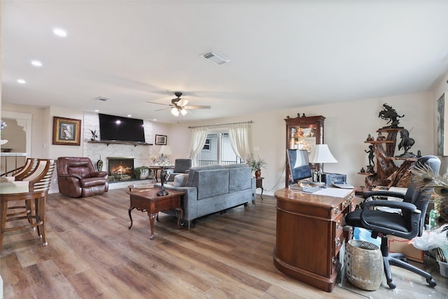 living room featuring ceiling fan, a large fireplace, and hardwood / wood-style floors