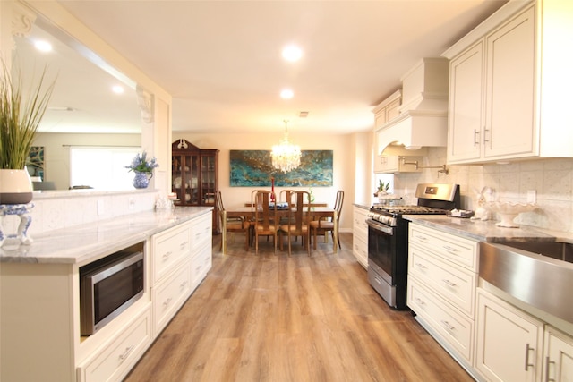 kitchen with custom exhaust hood, appliances with stainless steel finishes, light hardwood / wood-style floors, hanging light fixtures, and an inviting chandelier