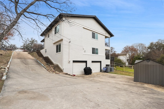 view of side of property featuring stairway, a shed, concrete driveway, a garage, and brick siding