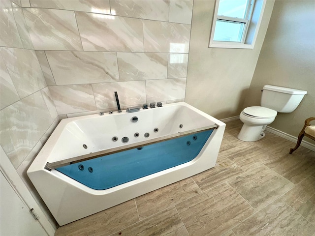 full bath with baseboards, toilet, and a tub with jets