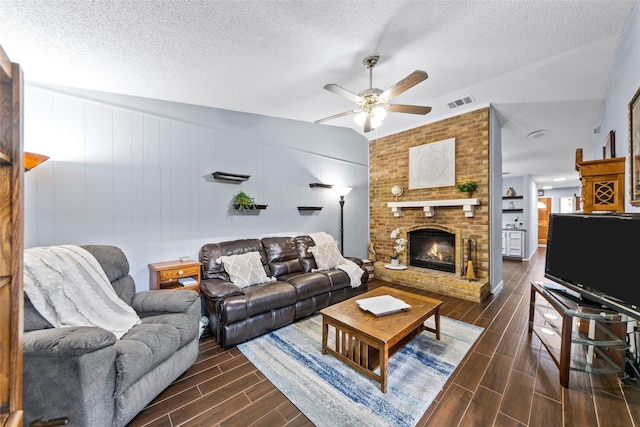 living room with lofted ceiling, a fireplace, a textured ceiling, and ceiling fan