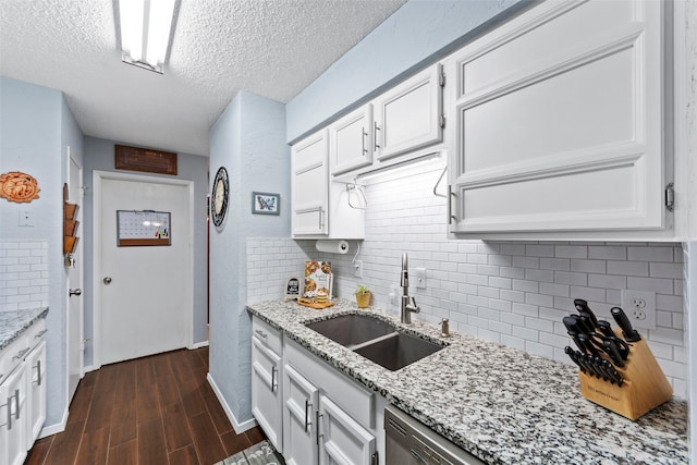 kitchen with light stone counters, a textured ceiling, white cabinetry, and sink