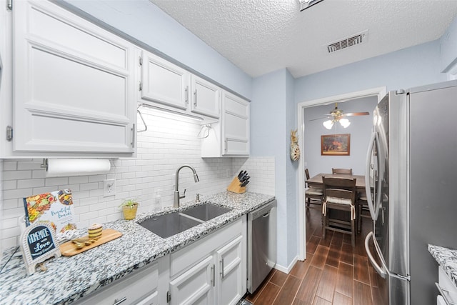 kitchen featuring light stone counters, stainless steel appliances, white cabinets, ceiling fan, and sink