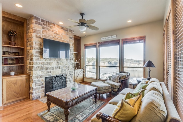 living room featuring light hardwood / wood-style floors, ceiling fan, built in features, and a fireplace