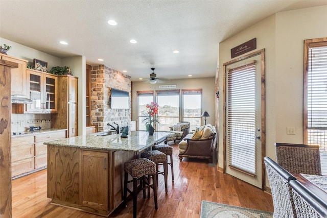 kitchen with sink, a center island with sink, wood-type flooring, and a breakfast bar