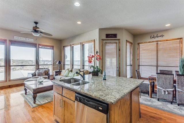 kitchen with light stone counters, dishwasher, light hardwood / wood-style floors, a kitchen island with sink, and sink