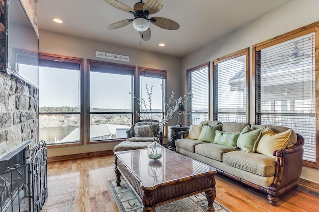 living room featuring a stone fireplace, ceiling fan, a water view, and light hardwood / wood-style flooring