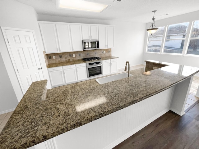 kitchen with appliances with stainless steel finishes, hanging light fixtures, white cabinetry, and dark stone countertops