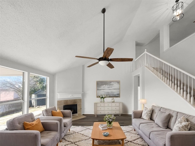 living room with a textured ceiling, lofted ceiling, a tiled fireplace, ceiling fan with notable chandelier, and dark hardwood / wood-style floors